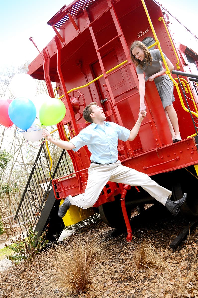 Red train caboose engagement pictures holding balloons and jumping in Clemson, SC